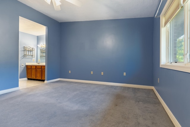 unfurnished bedroom featuring ceiling fan, ensuite bath, and light carpet