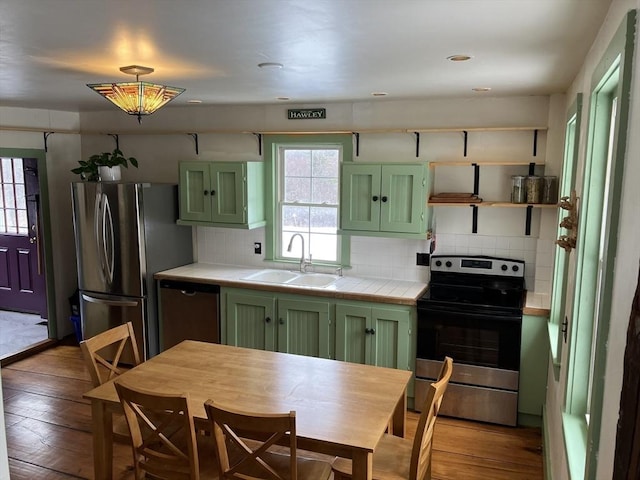 kitchen with stainless steel appliances, a sink, a healthy amount of sunlight, green cabinets, and tile counters