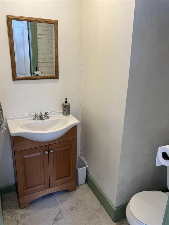 bathroom with toilet, marble finish floor, vanity, and baseboards