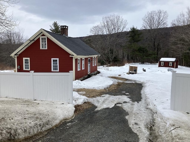 snow covered property with a chimney, an outdoor structure, and fence