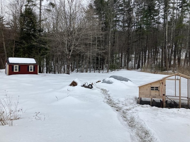 yard layered in snow with a forest view and an outbuilding