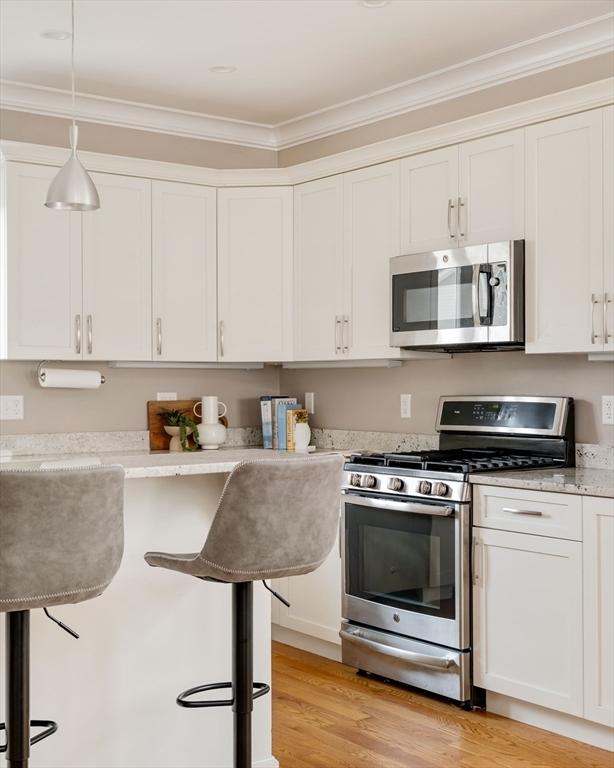 31 Neponset Ave, Boston, MA 02131 - kitchen featuring stainless steel appliances, crown molding, white cabinets, light wood-style floors, and hanging light fixtures