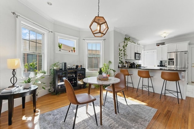 dining area featuring light wood-style floors, ornamental molding, and a healthy amount of sunlight