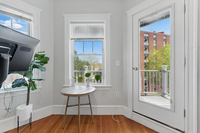 doorway to outside with baseboard heating, baseboards, a wealth of natural light, and wood finished floors