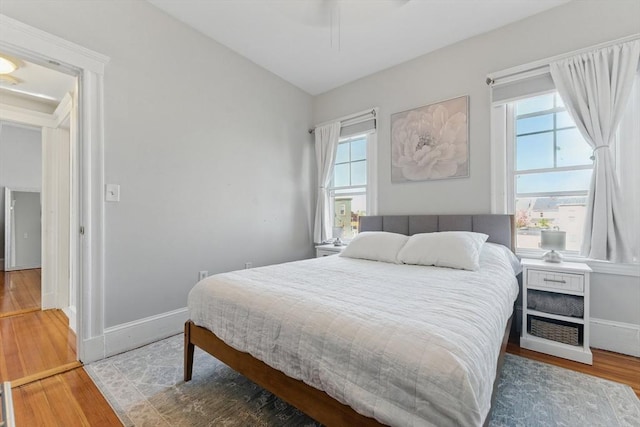 bedroom with baseboards, wood finished floors, and multiple windows