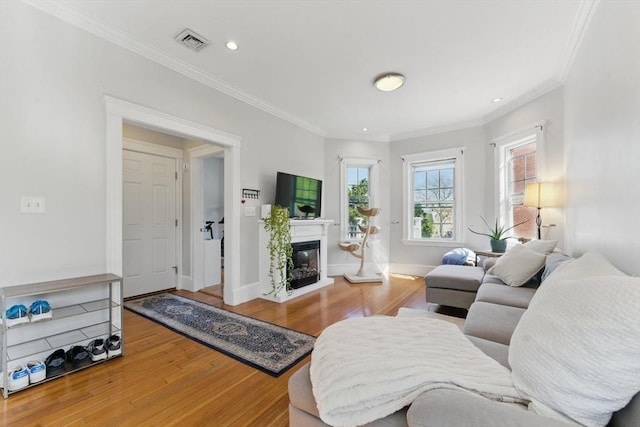 living room featuring visible vents, ornamental molding, a glass covered fireplace, and wood finished floors