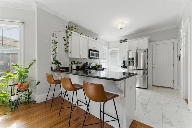 kitchen with a peninsula, dark countertops, a breakfast bar area, white cabinetry, and stainless steel appliances