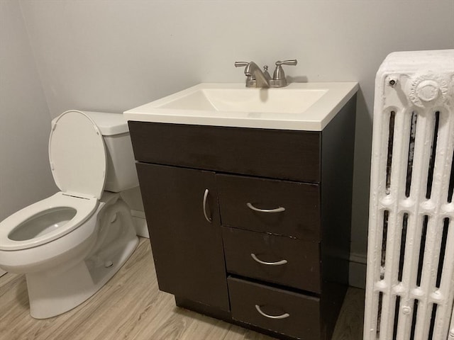 bathroom with hardwood / wood-style floors, vanity, toilet, and radiator