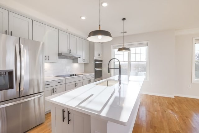 kitchen with pendant lighting, a wealth of natural light, a kitchen island with sink, and stainless steel appliances