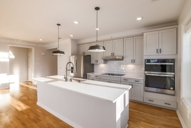 kitchen featuring a center island with sink, light hardwood / wood-style flooring, hanging light fixtures, gray cabinets, and appliances with stainless steel finishes