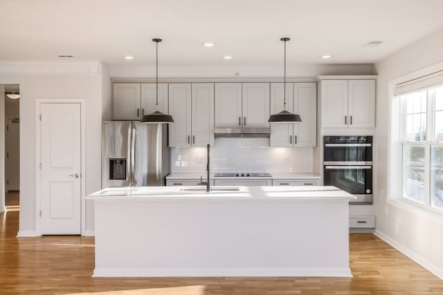 kitchen featuring light hardwood / wood-style floors, a kitchen island with sink, appliances with stainless steel finishes, and decorative light fixtures