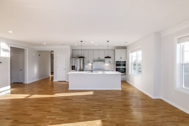 kitchen with a kitchen island with sink, stainless steel refrigerator with ice dispenser, black double oven, and hardwood / wood-style flooring