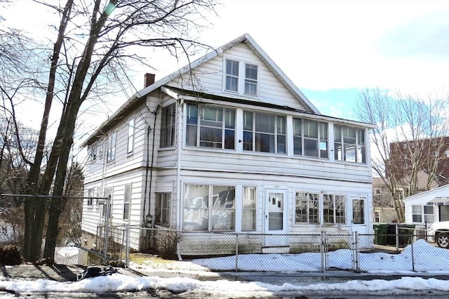 view of front facade with a fenced front yard, a sunroom, a chimney, and a gate