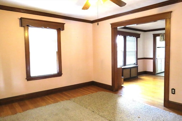 unfurnished room featuring wood finished floors, a ceiling fan, baseboards, ornamental molding, and radiator heating unit