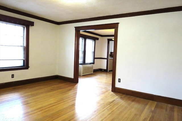 spare room featuring crown molding, radiator heating unit, light wood-style flooring, and baseboards