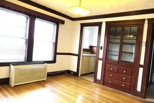 spare room with ornamental molding, radiator, baseboards, and light wood finished floors