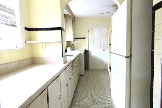 kitchen featuring arched walkways, light countertops, a ceiling fan, freestanding refrigerator, and a sink