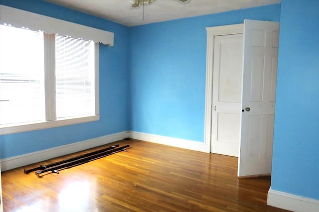 empty room with wood finished floors, a ceiling fan, and baseboards