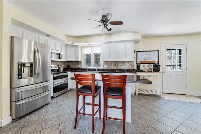 kitchen featuring a kitchen island, appliances with stainless steel finishes, white cabinetry, a breakfast bar area, and decorative backsplash