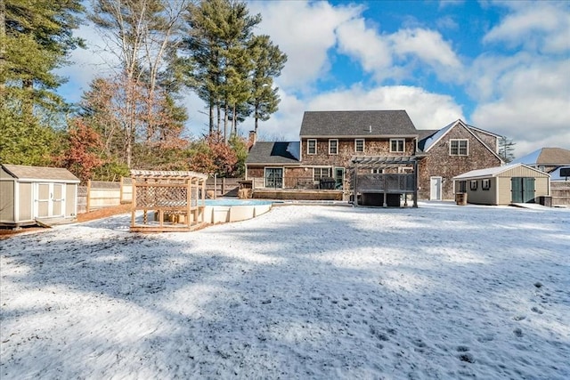 snow covered house featuring a storage unit, a covered pool, and a pergola