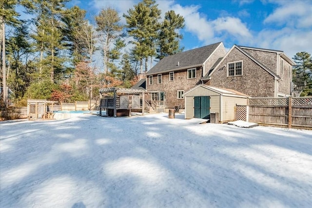 snow covered rear of property featuring a pergola and a shed