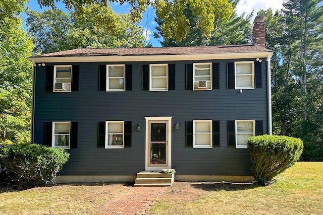 colonial house with entry steps, a chimney, and a front lawn