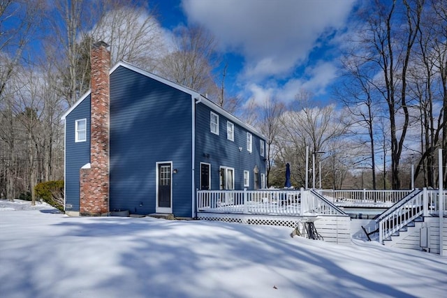 view of snowy exterior with a deck, a chimney, and stairs