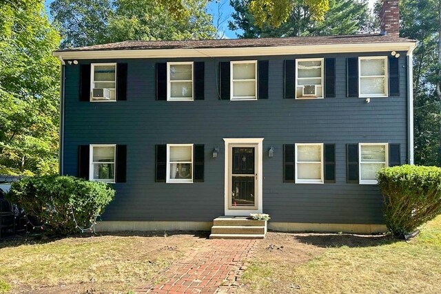 colonial house with a front lawn, a chimney, and cooling unit