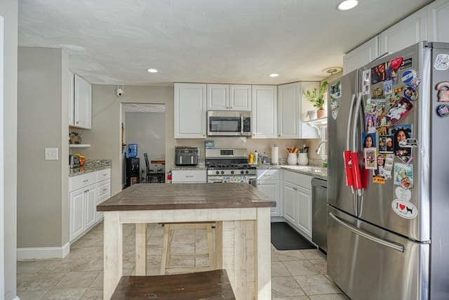 kitchen with light tile patterned floors, appliances with stainless steel finishes, white cabinetry, and light stone countertops