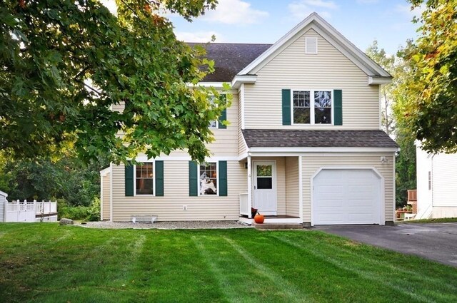traditional-style home with an attached garage, a shingled roof, a front lawn, and driveway