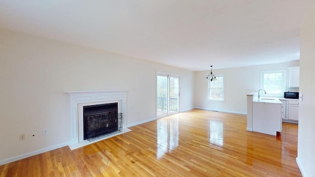 unfurnished living room with light wood-style flooring, a fireplace with flush hearth, baseboards, and a sink