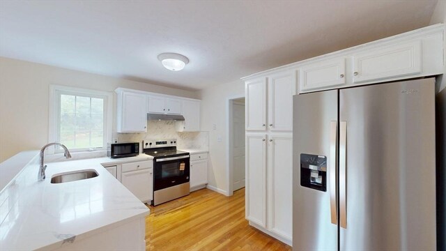 kitchen featuring appliances with stainless steel finishes, a sink, under cabinet range hood, white cabinetry, and backsplash