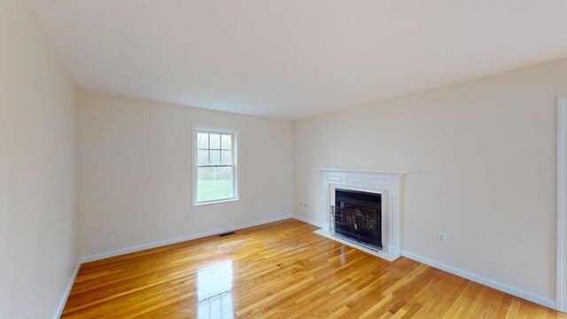 unfurnished living room featuring light wood-style flooring, a fireplace with flush hearth, and baseboards