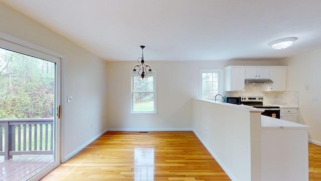 kitchen featuring stainless steel electric stove, light wood-style floors, under cabinet range hood, white cabinets, and backsplash