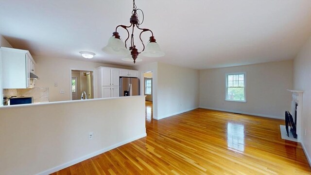 unfurnished living room featuring a fireplace with flush hearth, baseboards, and light wood-style floors