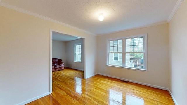 empty room featuring plenty of natural light, crown molding, light wood-style floors, baseboards, and a textured ceiling