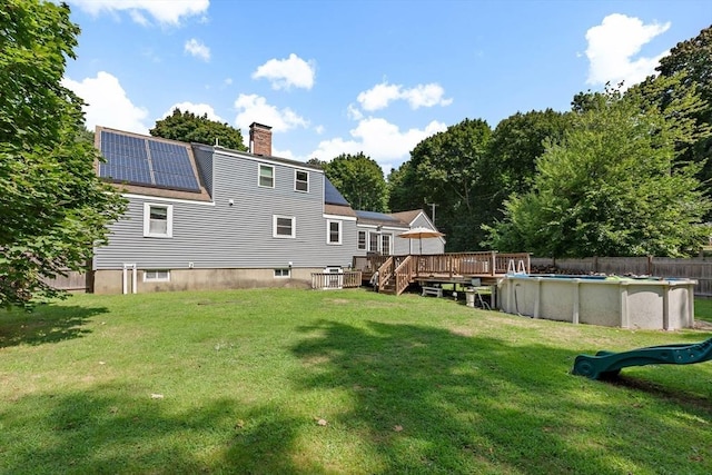 2 Woodbrier Rd, Topsfield, MA 01983 - rear view of property featuring a wooden deck, a yard, a chimney, an outdoor pool, and roof mounted solar panels