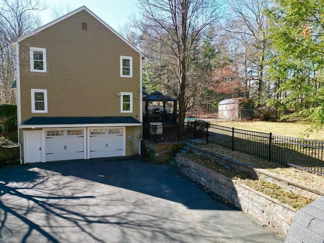 view of property exterior featuring aphalt driveway, a garage, and fence