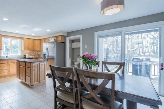 kitchen with light tile patterned flooring, a sink, stainless steel fridge, backsplash, and a center island