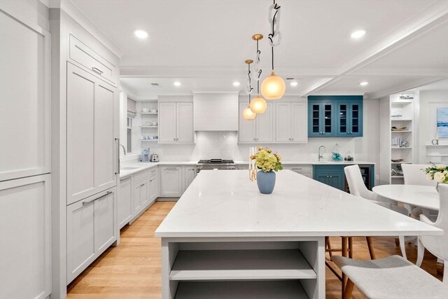 kitchen with light wood finished floors, open shelves, a kitchen island, premium range hood, and a sink