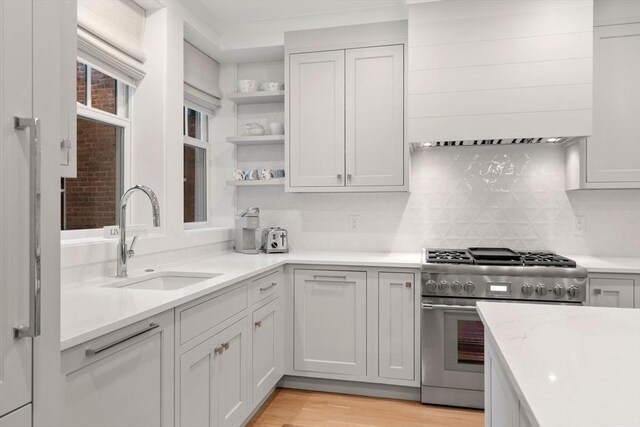 kitchen with a sink, light countertops, stainless steel stove, custom exhaust hood, and open shelves