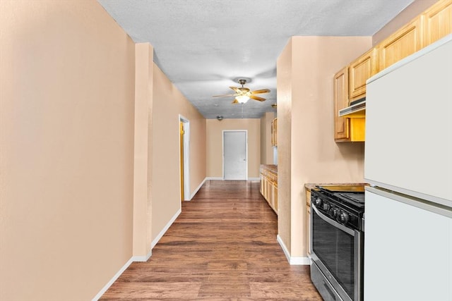 kitchen featuring stainless steel gas range oven, light brown cabinets, wood finished floors, baseboards, and freestanding refrigerator