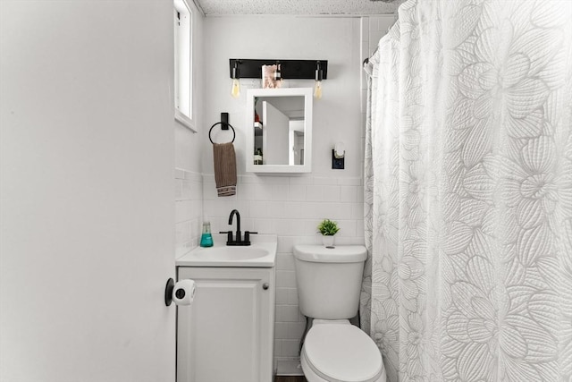 bathroom with tile walls, curtained shower, toilet, wainscoting, and vanity