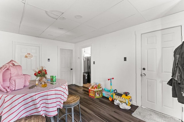 bedroom with dark wood-style flooring, a drop ceiling, freestanding refrigerator, and baseboards