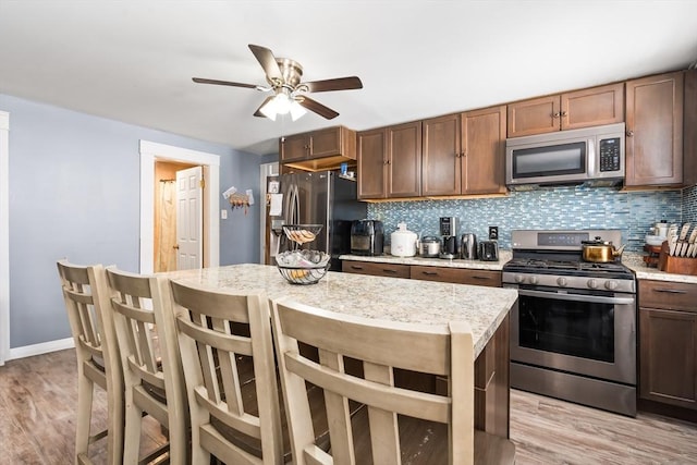 kitchen featuring appliances with stainless steel finishes, light wood-style floors, decorative backsplash, and a kitchen bar