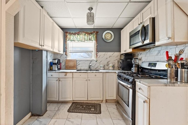 kitchen featuring light countertops, backsplash, stainless steel appliances, marble finish floor, and a sink