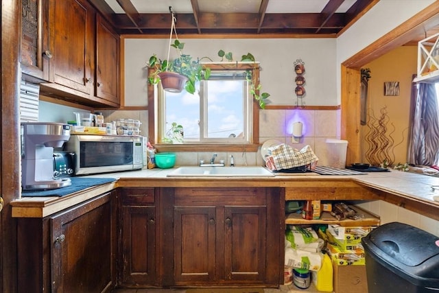 kitchen featuring beamed ceiling, tasteful backsplash, stainless steel microwave, a sink, and tile counters