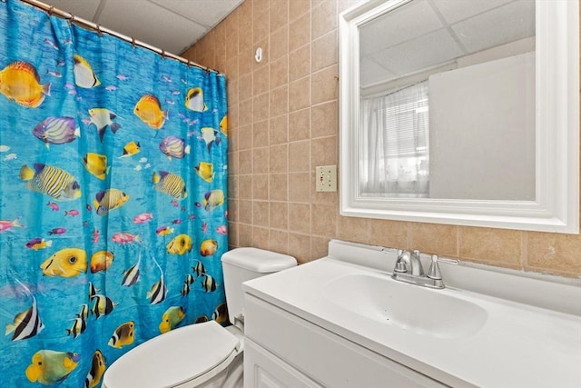 full bathroom with vanity, a drop ceiling, toilet, curtained shower, and tile walls