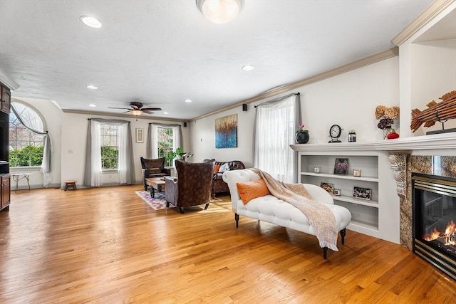living room featuring a fireplace, crown molding, light wood-style flooring, and recessed lighting