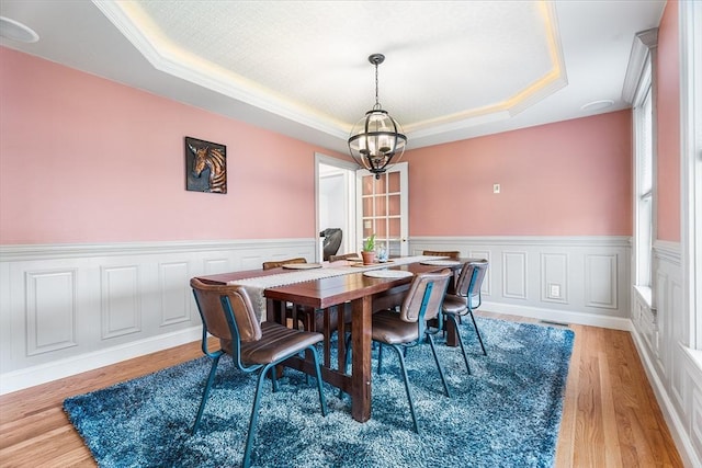 dining space with a chandelier, wainscoting, light wood finished floors, and a tray ceiling